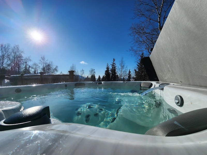 Hot tub with still water under clear blue sky with sun and tree line