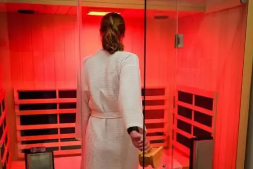 Woman wearing white robe entering a Jacuzzi brand red-light therapy Sauna.